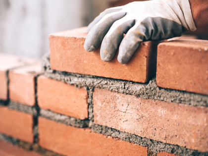 Gloved hands laying red bricks with mortar on a brick wall