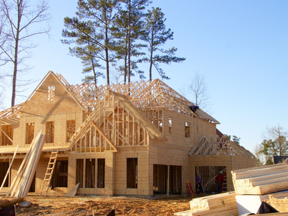 New house under construction with wooden framing and roof trusses on a sunny day