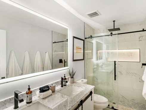 Modern bathroom with double sink, large mirror, glass shower, and white towels