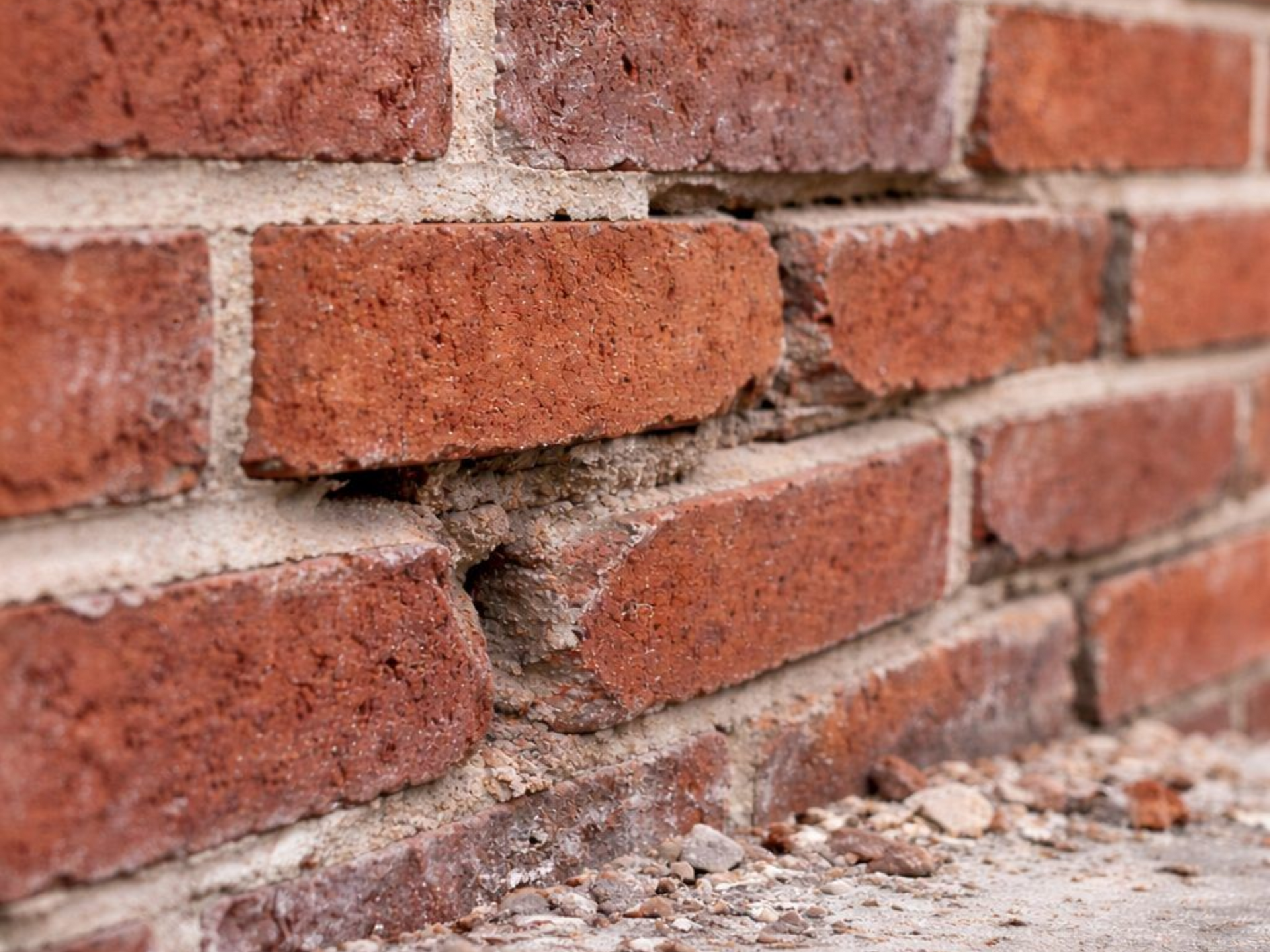 Damaged red brick wall with cracks and missing mortar at the base