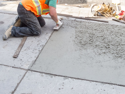 Worker in orange safety vest smoothing wet concrete at a construction site