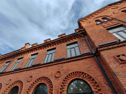 Low-angle view of a red brick historic building with arched windows against a cloudy sky