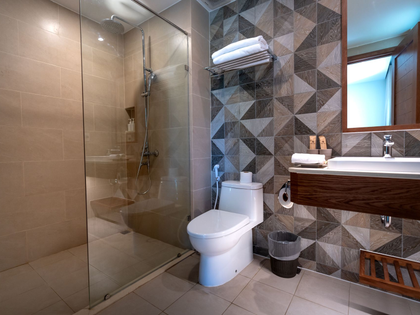 Modern bathroom with glass shower, white toilet, vanity, geometric accent wall, and window daylight
