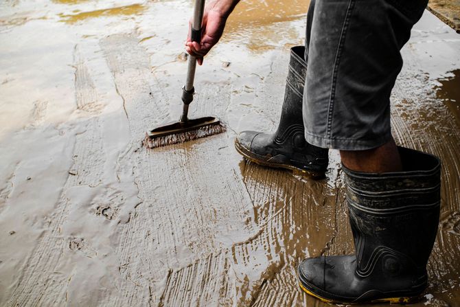 Person using a rake to smooth wet concrete while wearing black rubber boots.