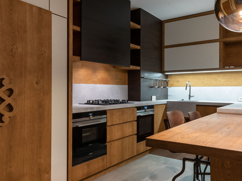 Modern kitchen with wood cabinets, black stove, sink, and dining table under warm lighting