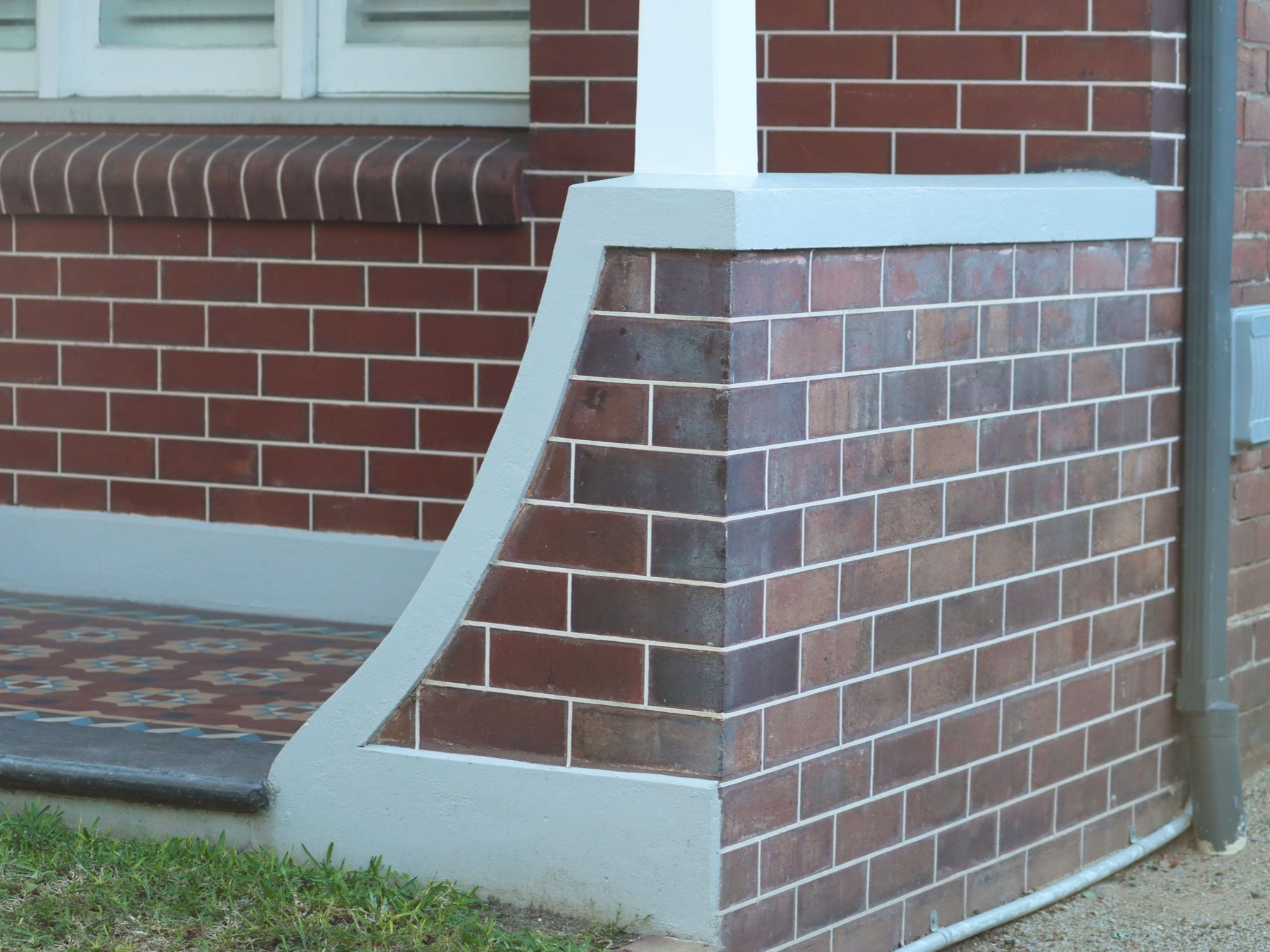 Brick house corner with a sloped concrete wheelchair ramp beside a window and steps