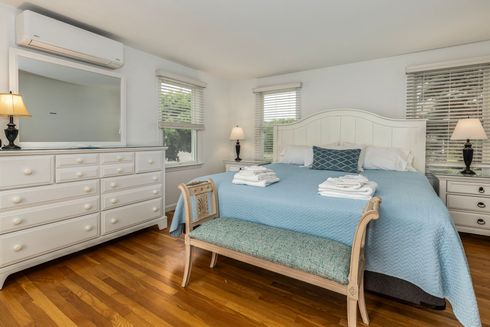 A bedroom with a king size bed , dresser , mirror and bench.