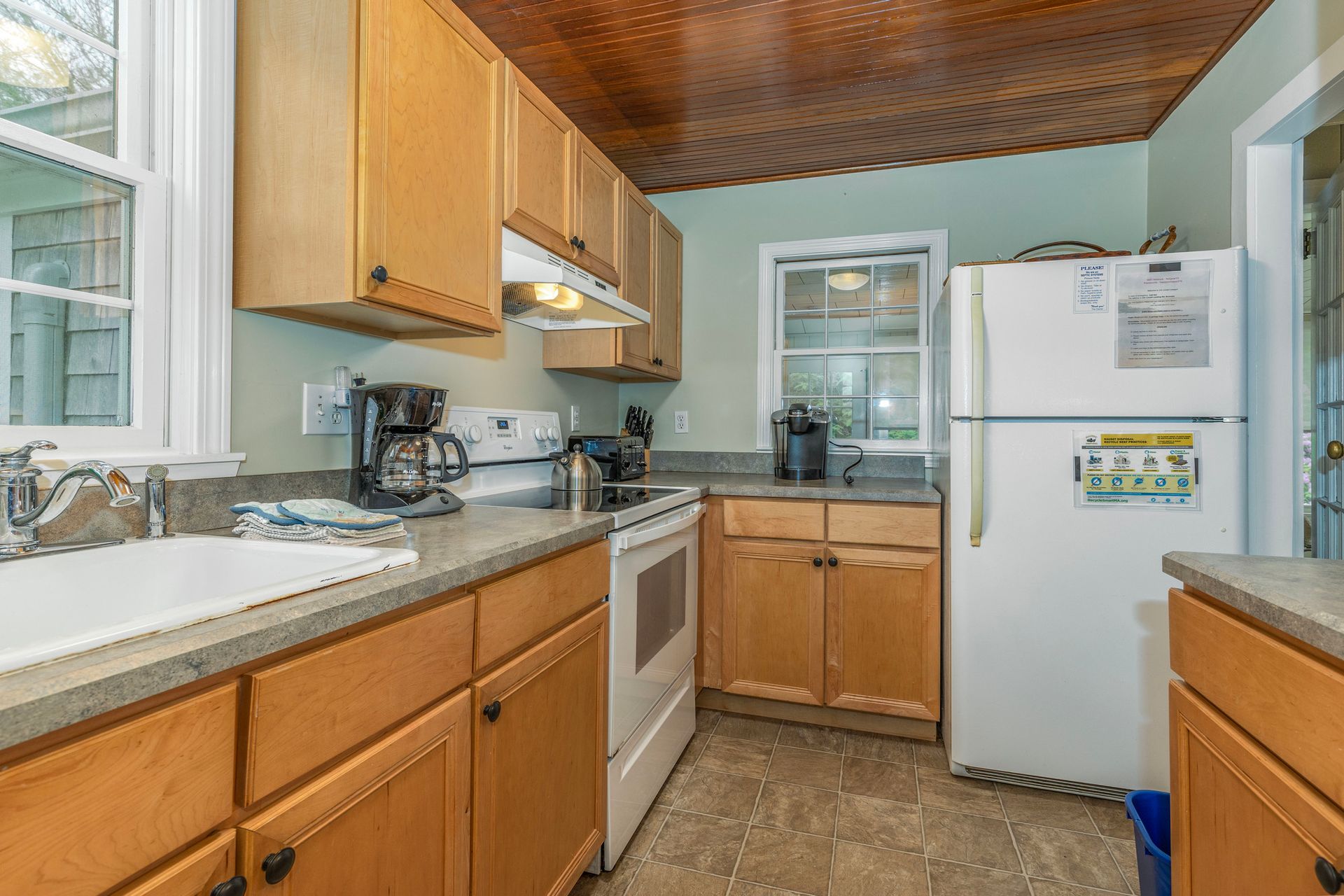 A kitchen with wooden cabinets , a white refrigerator , a stove , and a sink.