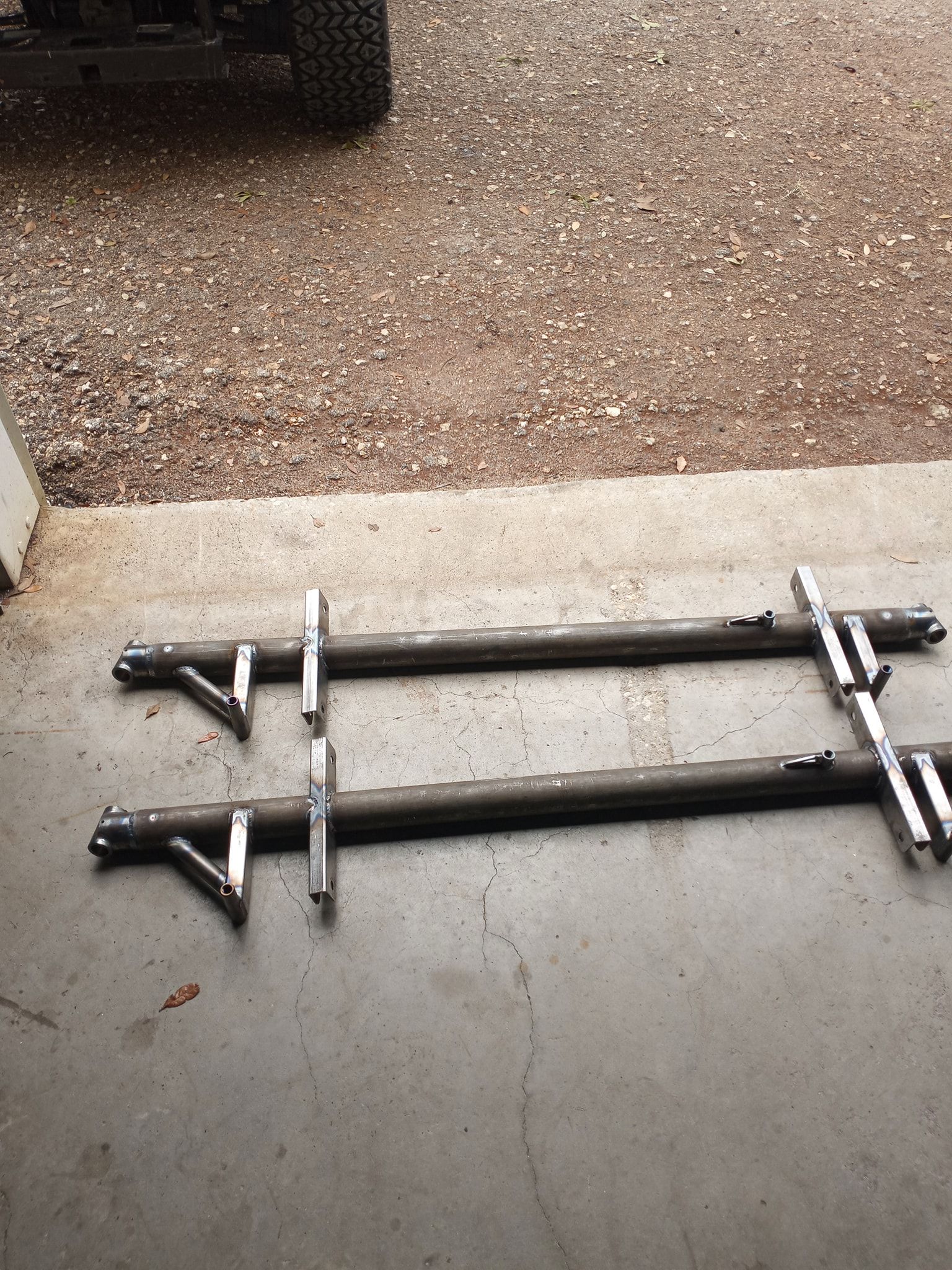 Two metal bars with welded brackets, lying on a concrete surface.