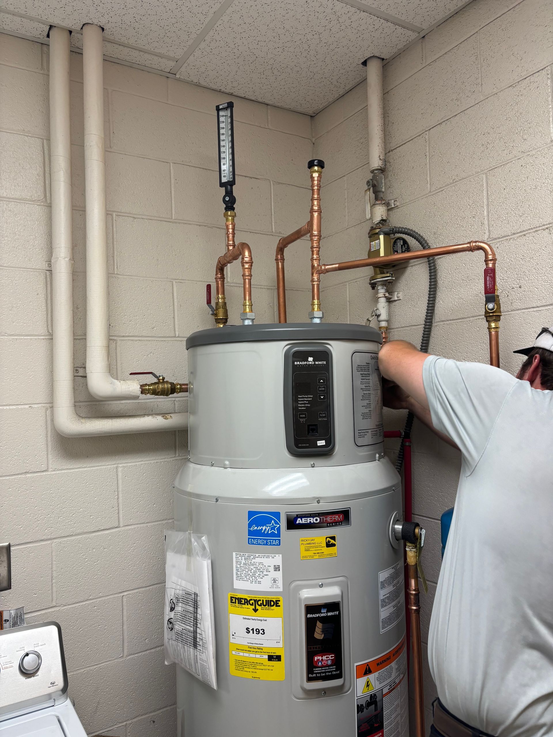 Person pointing at a water heater with copper pipes in a utility room