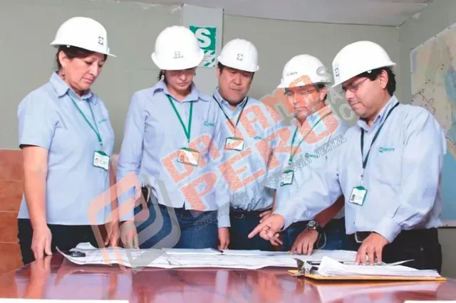 Cinco trabajadores con cascos blancos revisan planos en una mesa de oficina.