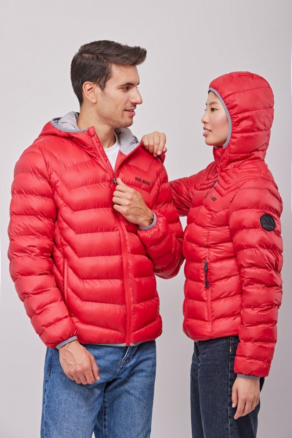 Dos personas con chaquetas acolchadas rojas están de pie una frente a la otra, una ajustándole el cuello a la otra.