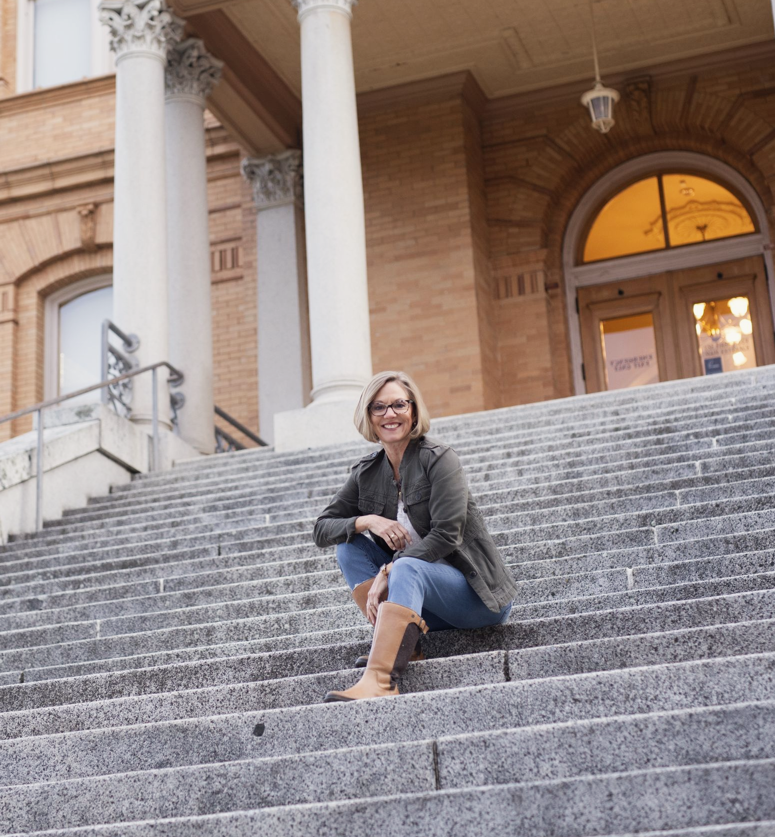 Joy Mitchell sitting on stone steps in front of a building with columns and a large arched doorway.