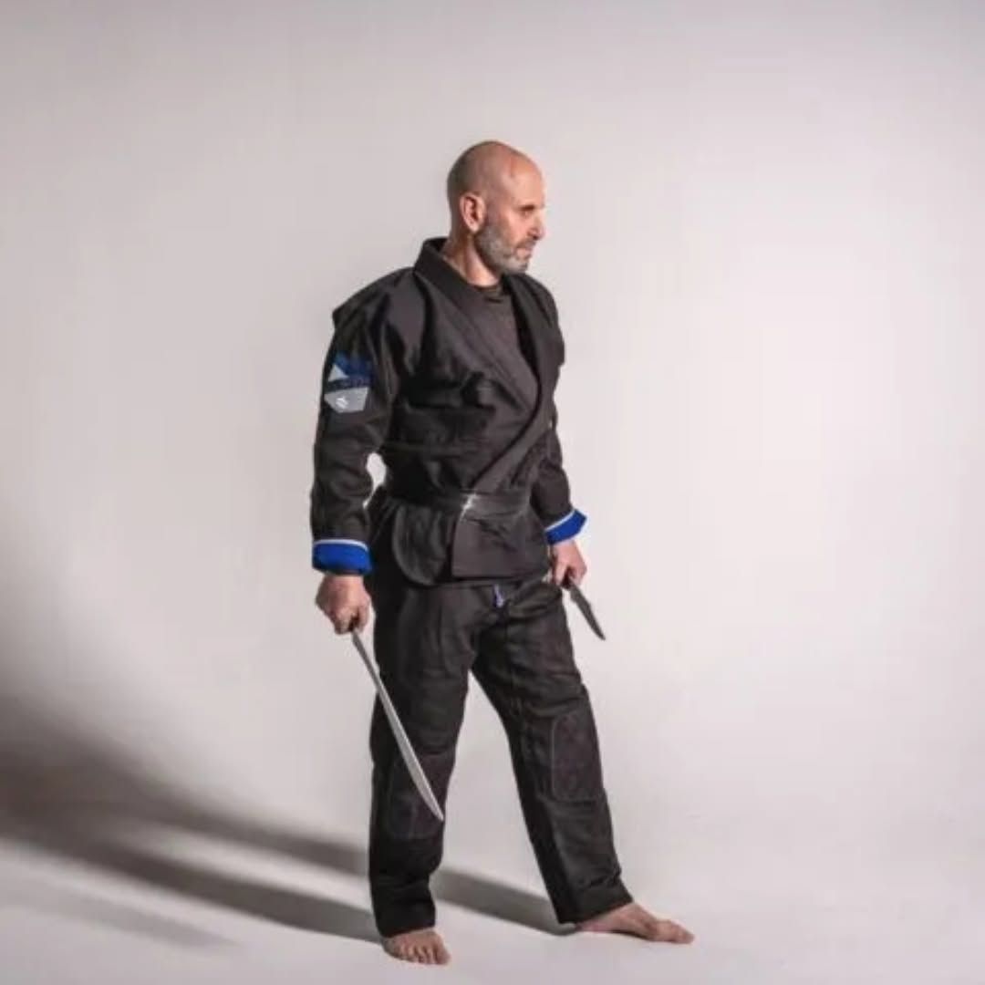 Person in a black martial arts uniform holding a sword, standing barefoot against a plain background