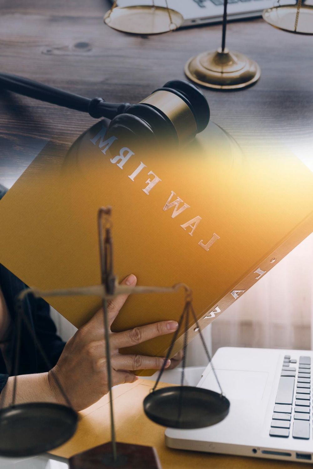 Law firm sign on desk beside a gavel, scales, and a hand holding glasses