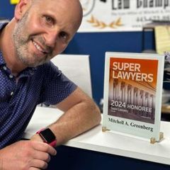 Man smiling beside a Super Lawyers 2024 honoree plaque on a desk in an office.