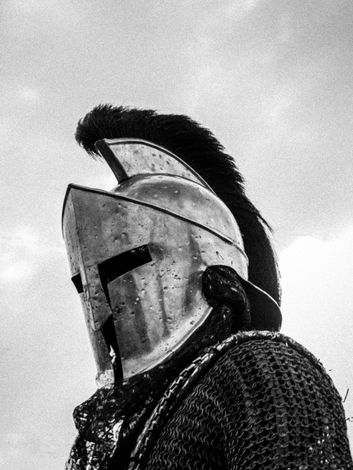 Close-up of a medieval knight in a plumed helmet and chainmail against a cloudy sky