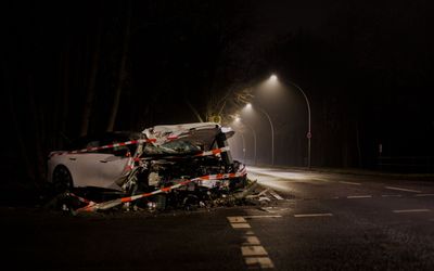 Severe crash with a wrecked car on a dark, wet road under streetlights at night