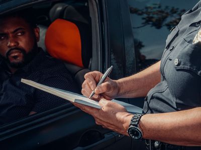 Officer writing a ticket through a car window while driver watches from inside