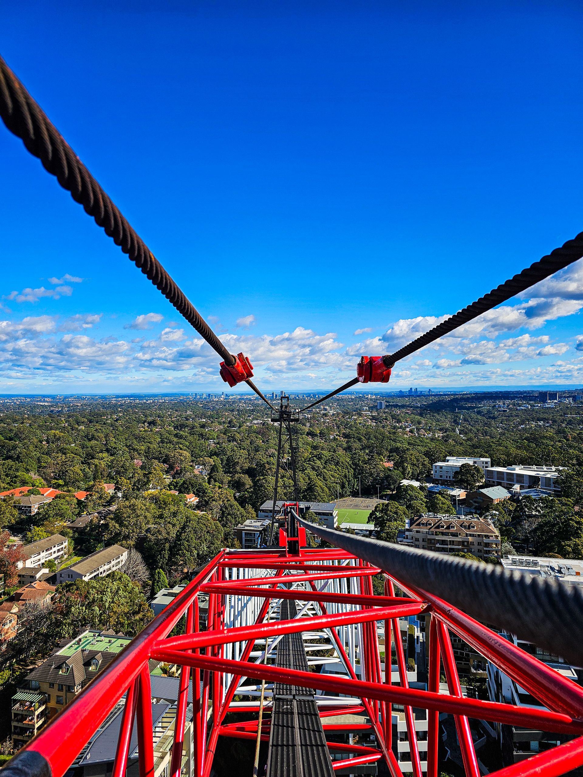Three construction workers in safety gear hoist a suspended cable bundle under a steel structure.