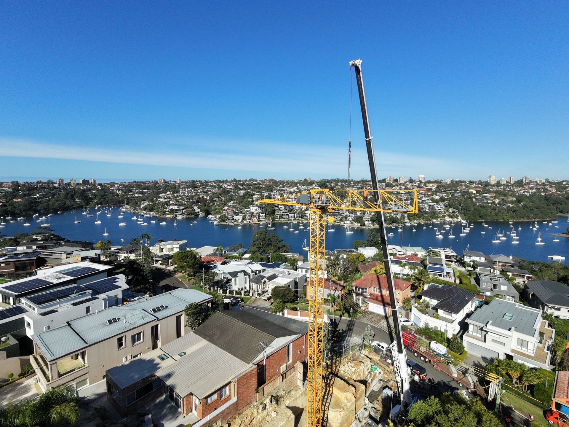 Tall yellow construction crane above a city skyline and active building site under a blue sky