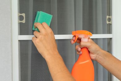 A person is cleaning a screen door with a sponge and spray bottle.