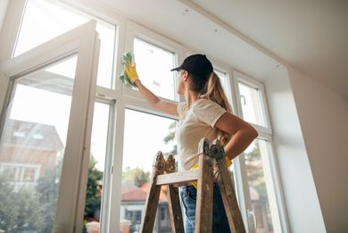 A woman is standing on a ladder cleaning a window.