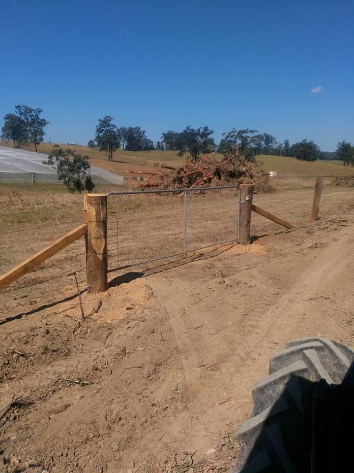 a Tractor is Driving Down a Dirt Road Next to a Wooden Fence — Tony Sinclair Fencing In Grafton, NSW