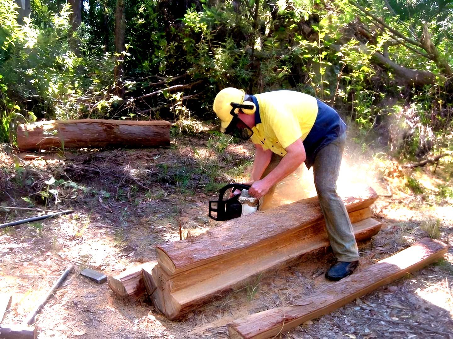 a Man is Using a Chainsaw to Cut a Log — Tony Sinclair Fencing In Grafton, NSW