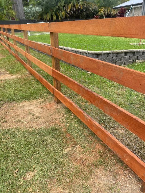 a Wooden Fence is Sitting in the Middle of a Lush Green Field — Tony Sinclair Fencing In Bellingen, NSW 
