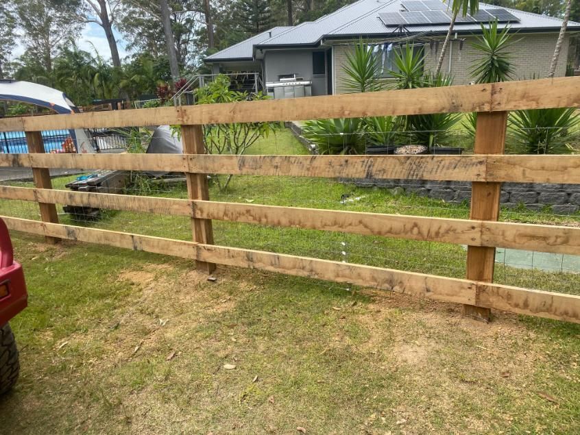 a Wooden Fence is Sitting in the Grass in Front of a House — Tony Sinclair Fencing In Bucca, NSW