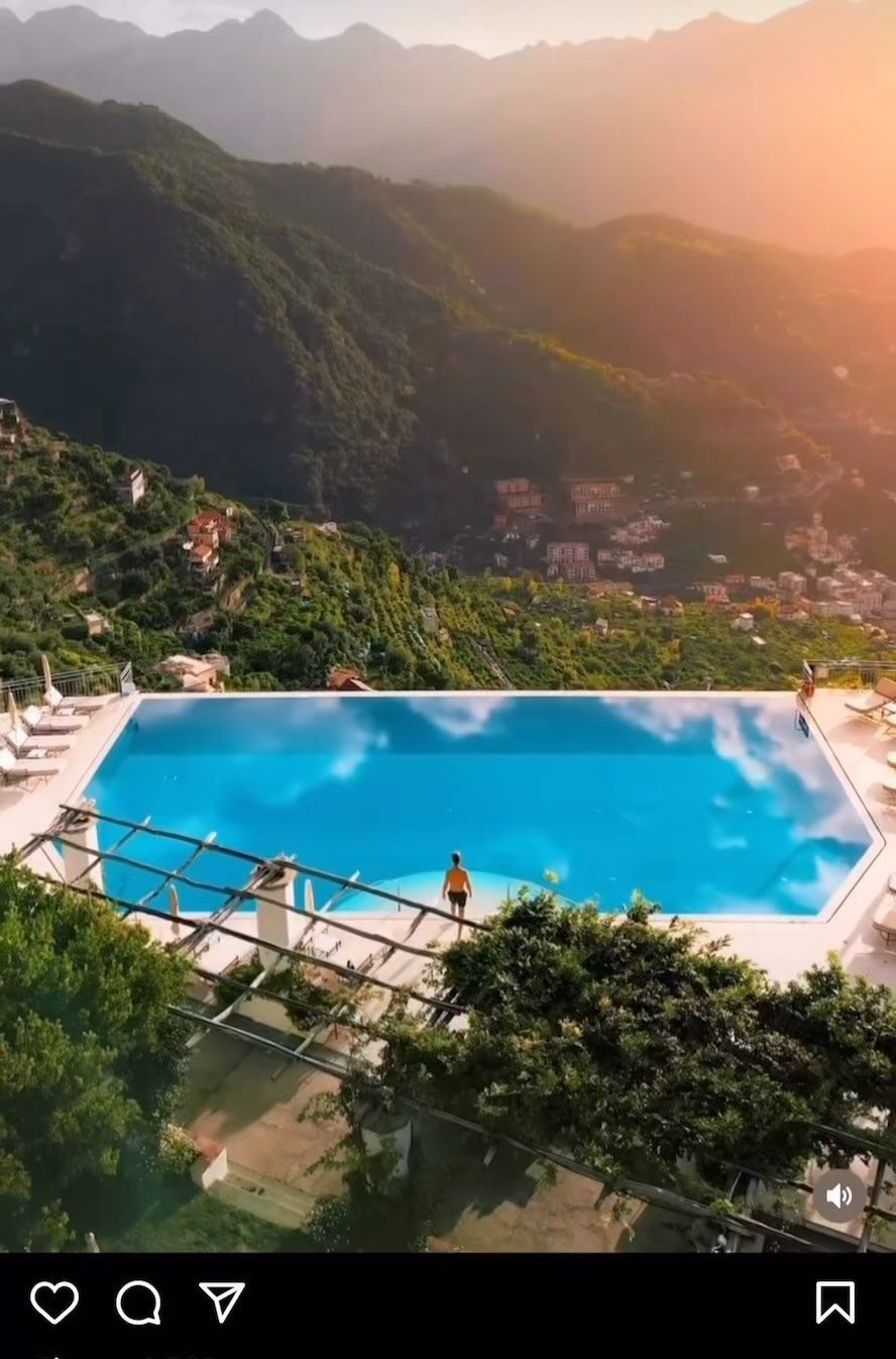 Piscina a sfioro con vista su una lussureggiante valle di montagna al tramonto, con cime nebbiose sullo sfondo.