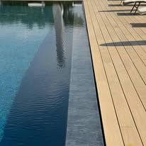 Piscina blu accanto a una terrazza in legno chiaro con lettini prendisole.