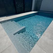 Moderna piscina all'aperto con acqua cristallina e zona relax poco profonda.