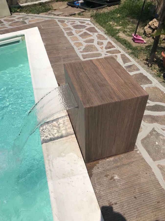 Panchina in legno a bordo piscina, accanto all'acqua turchese e al sentiero in pietra.