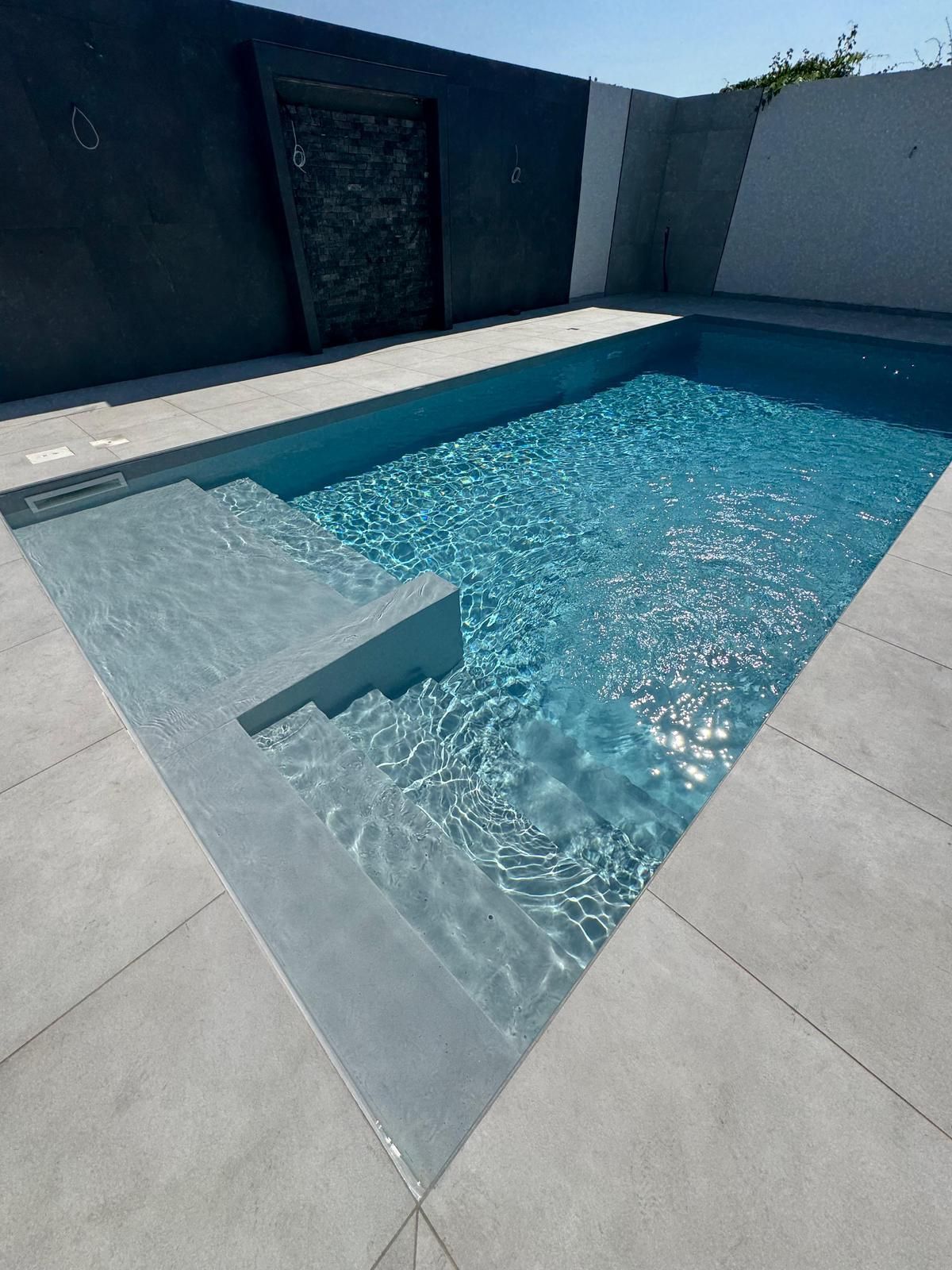 Moderna piscina da giardino con acqua cristallina e pavimentazione in pietra chiara.