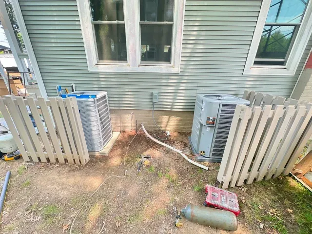 A house with two air conditioners on the side of it next to a fence.