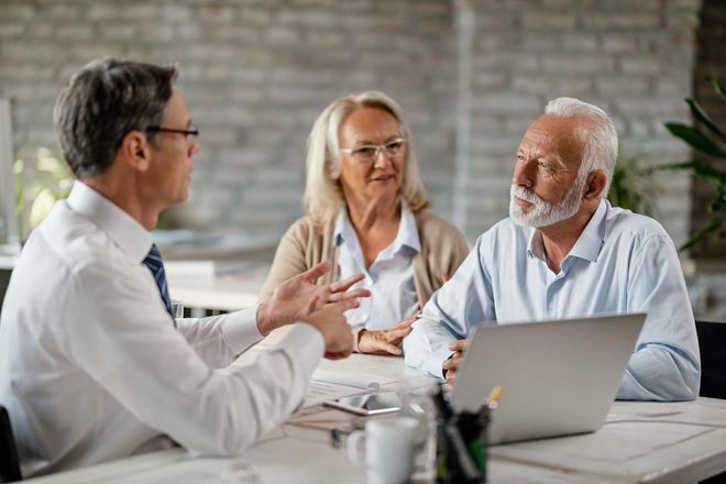 Three people in a meeting discussing documents at a table with a laptop in a bright office