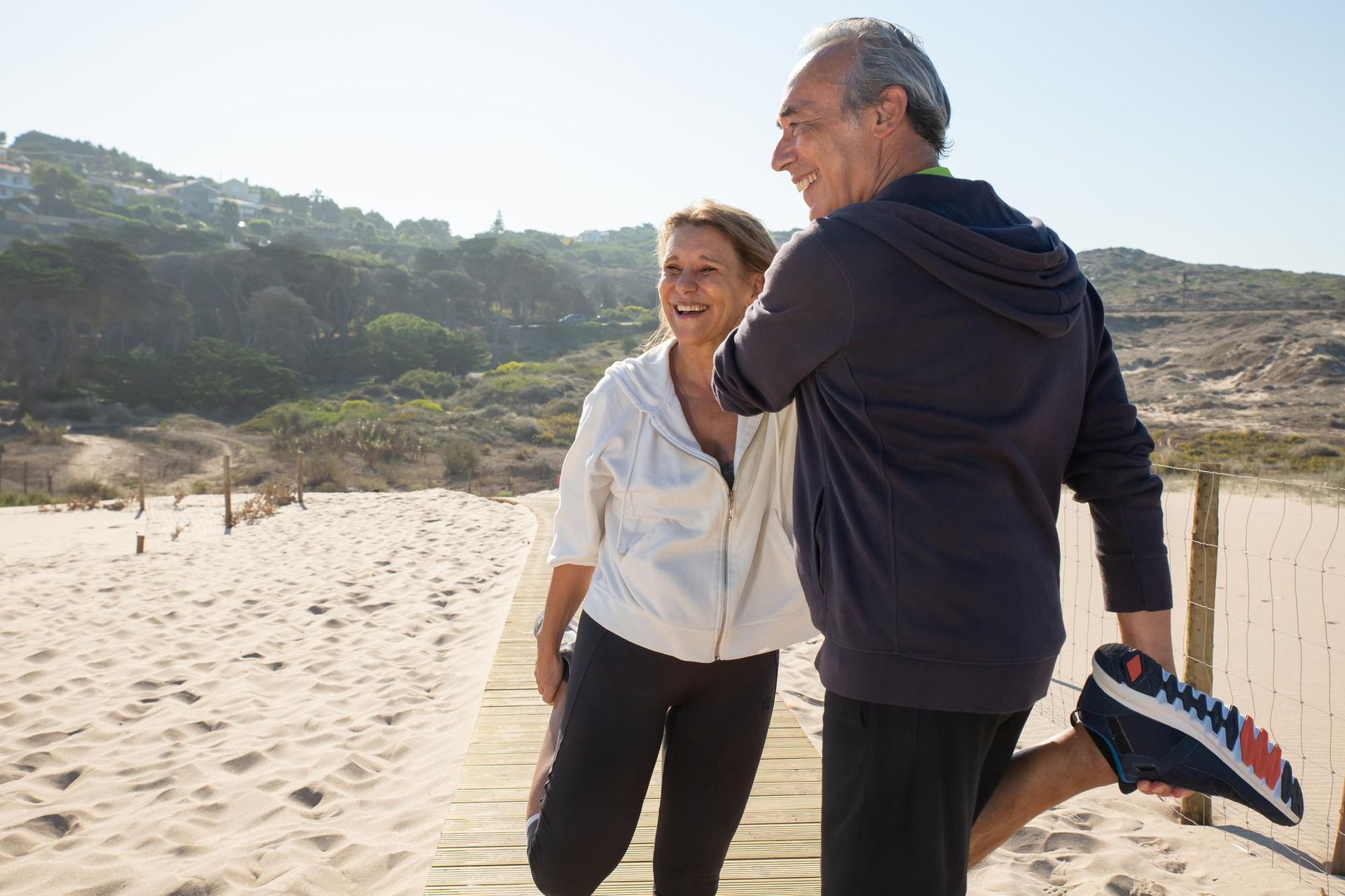 Two people standing on a sunny sandy beach, smiling and holding a surfboard.