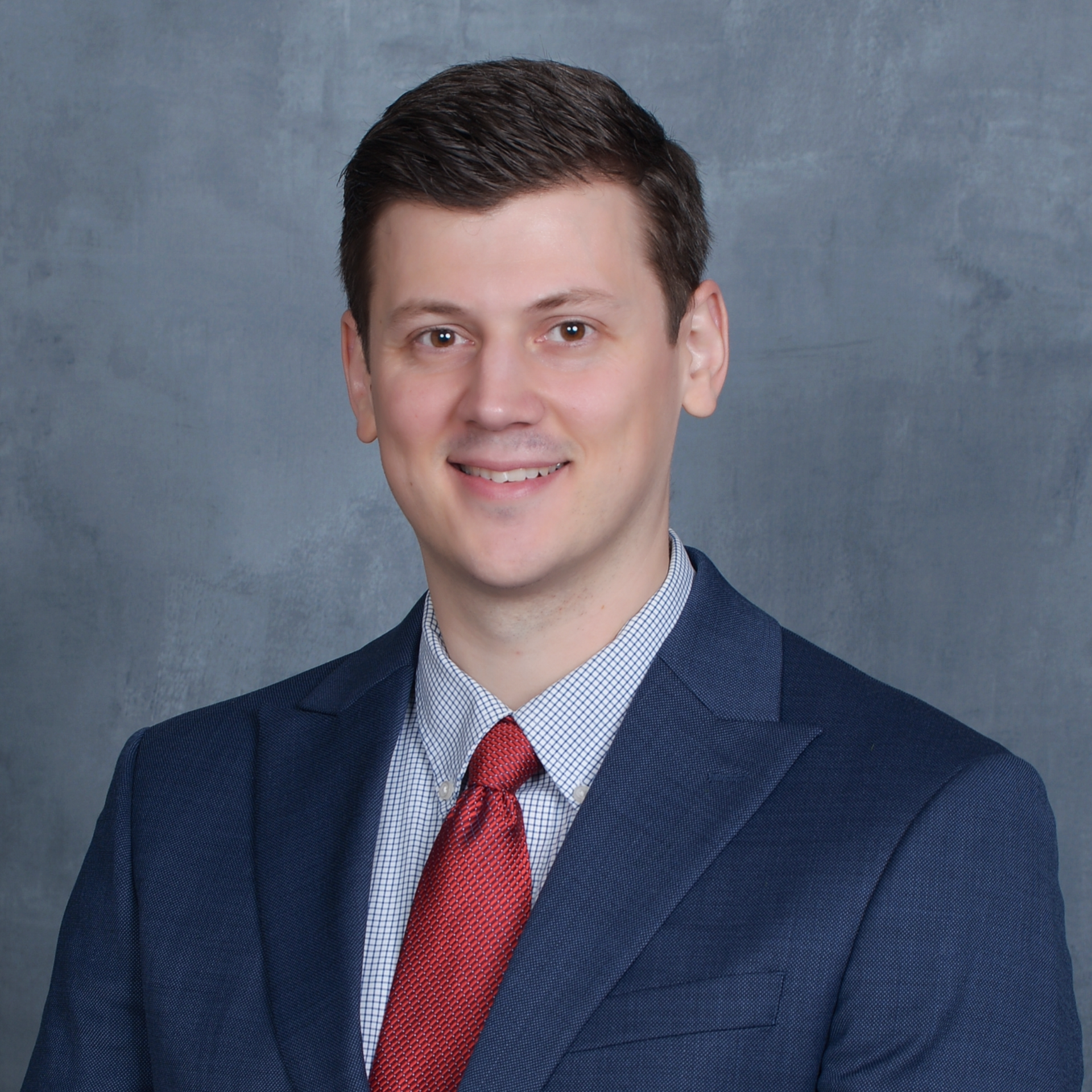Ryan Olson in a navy suit and red tie against a gray background