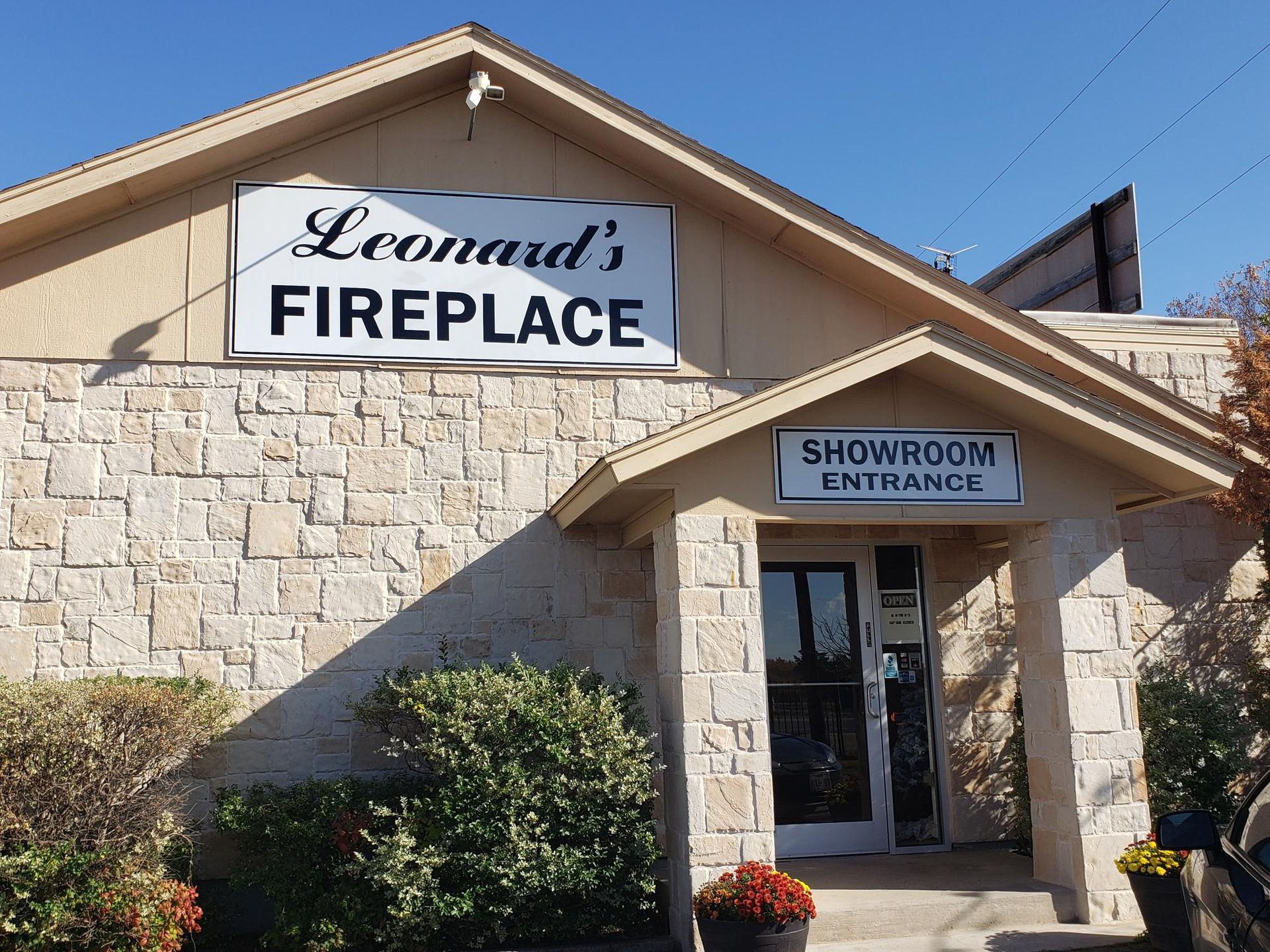 The stone exterior of Leonard's Fireplace storefront under a bright blue sky, with a sign reading