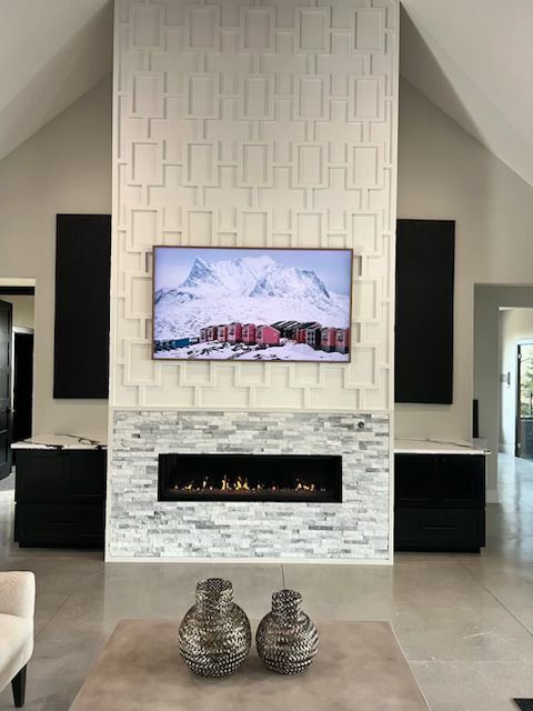 A modern living room features a fireplace wall with a stone base, a geometric white upper section, and a mounted TV.