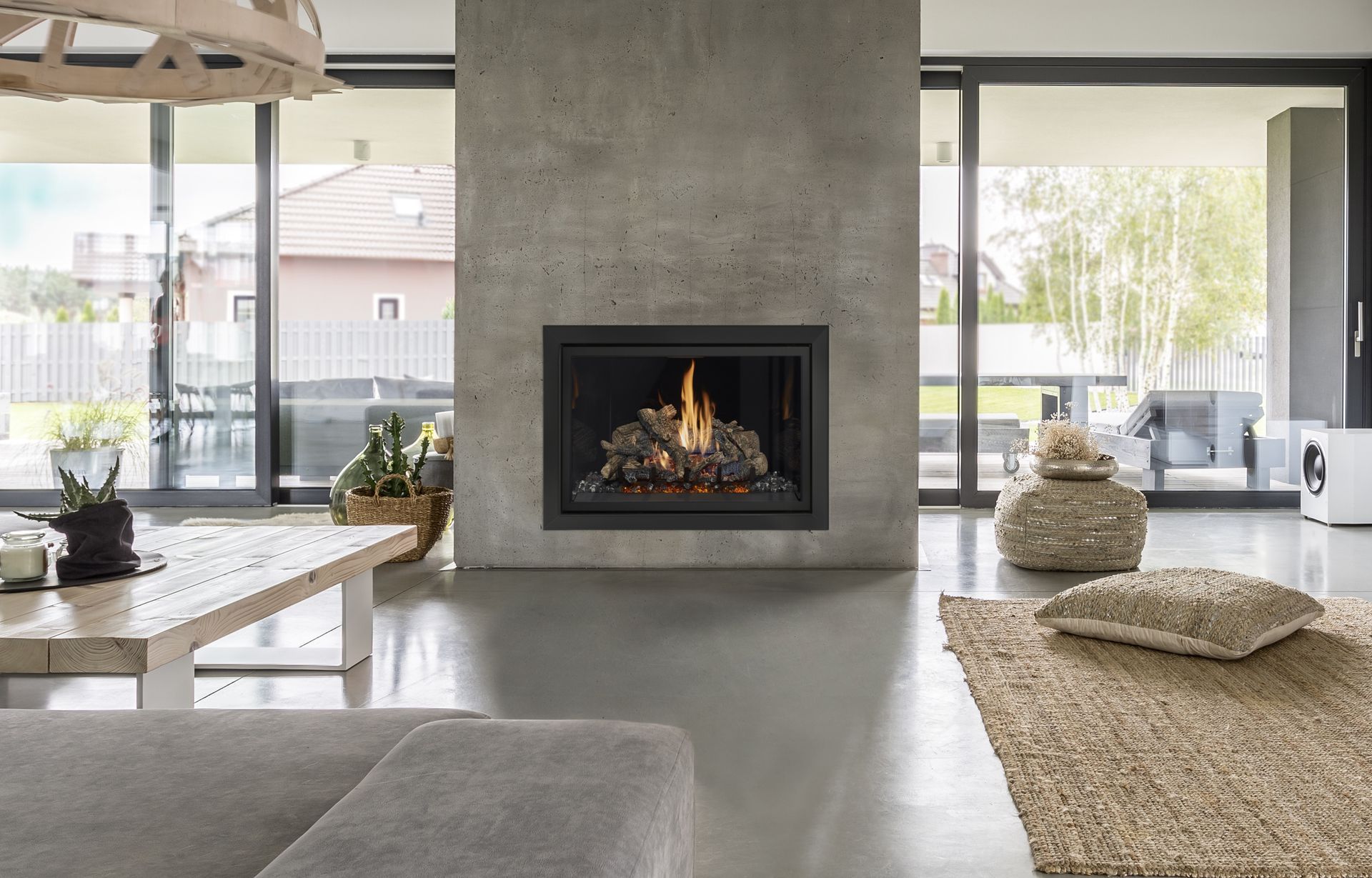 A modern living room with a concrete fireplace, a wooden coffee table, a jute rug, and glass doors opening to a patio.