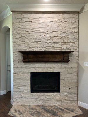 A fireplace featuring a dark wood mantel set against a textured, light cream-colored stone wall.