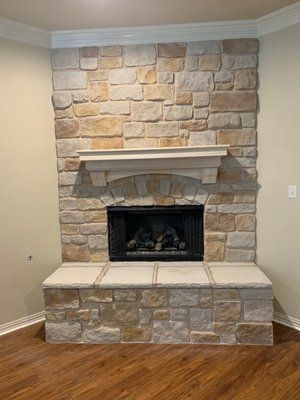 A floor-to-ceiling stone fireplace with a light-colored stone hearth and mantel, set against neutral beige walls.