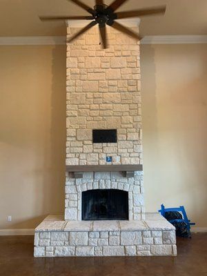 A tall, floor-to-ceiling stone fireplace with a thick mantel, centered in a room with a ceiling fan.