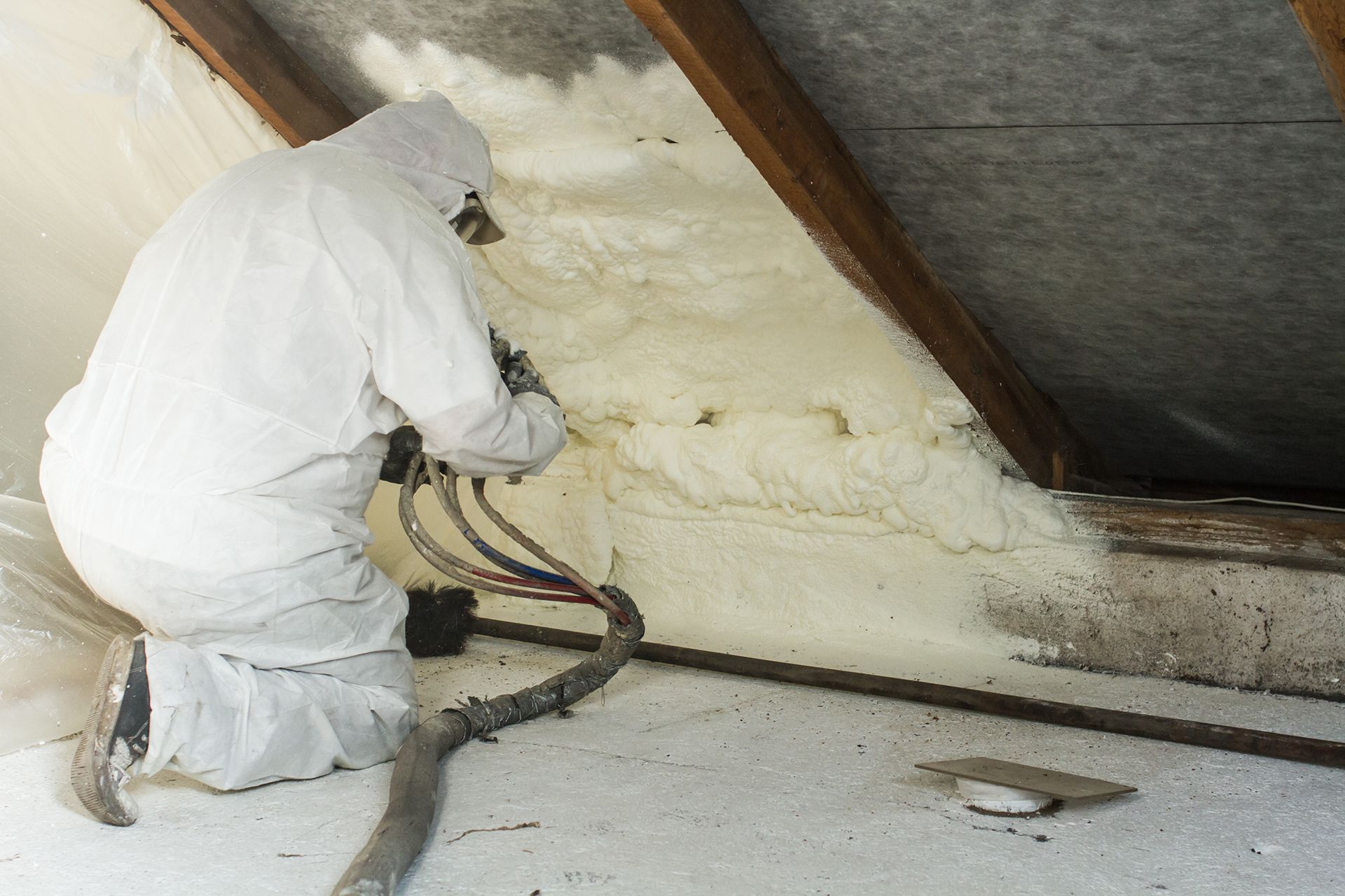A man in a white suit is spraying foam on a wall.