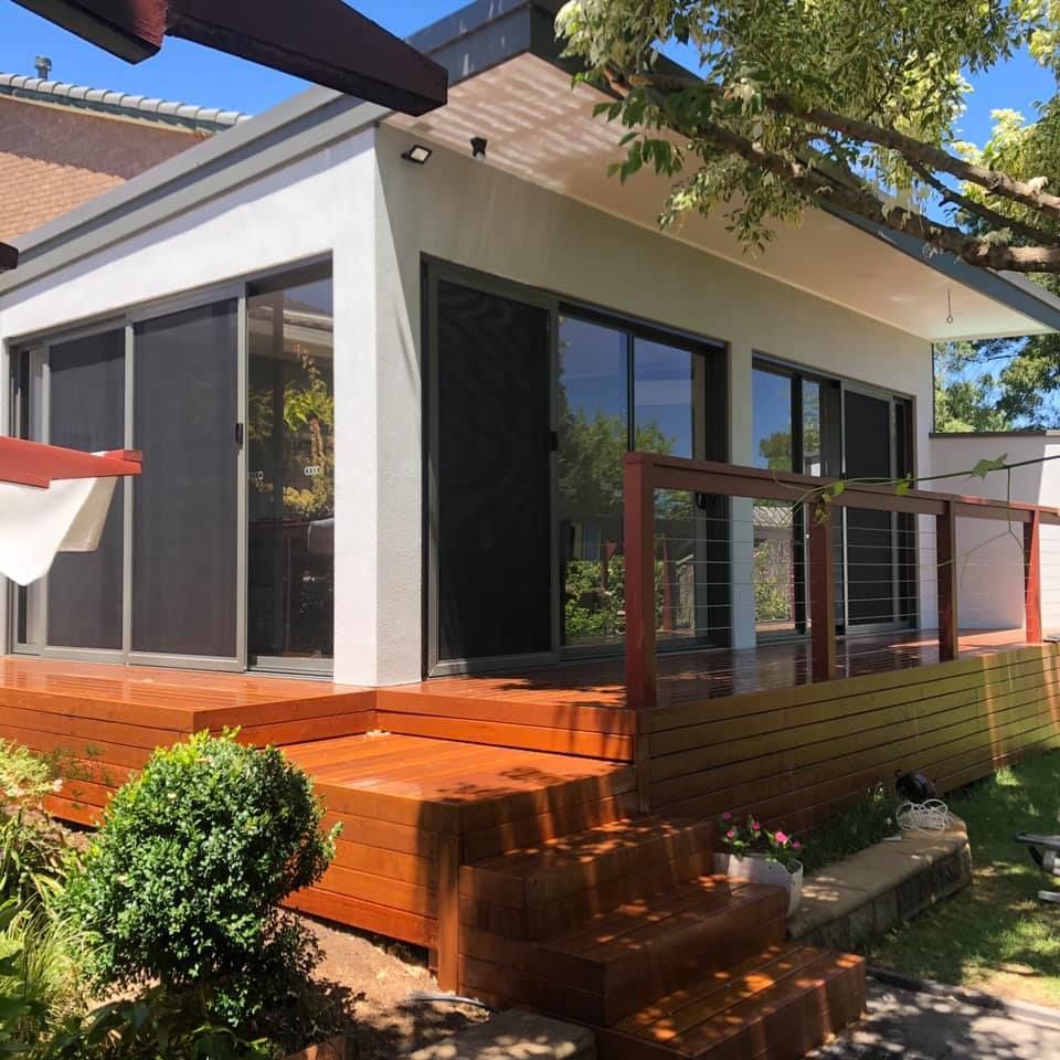 A wooden carport frame under construction attached to a house, with building materials scattered on the concrete patio.