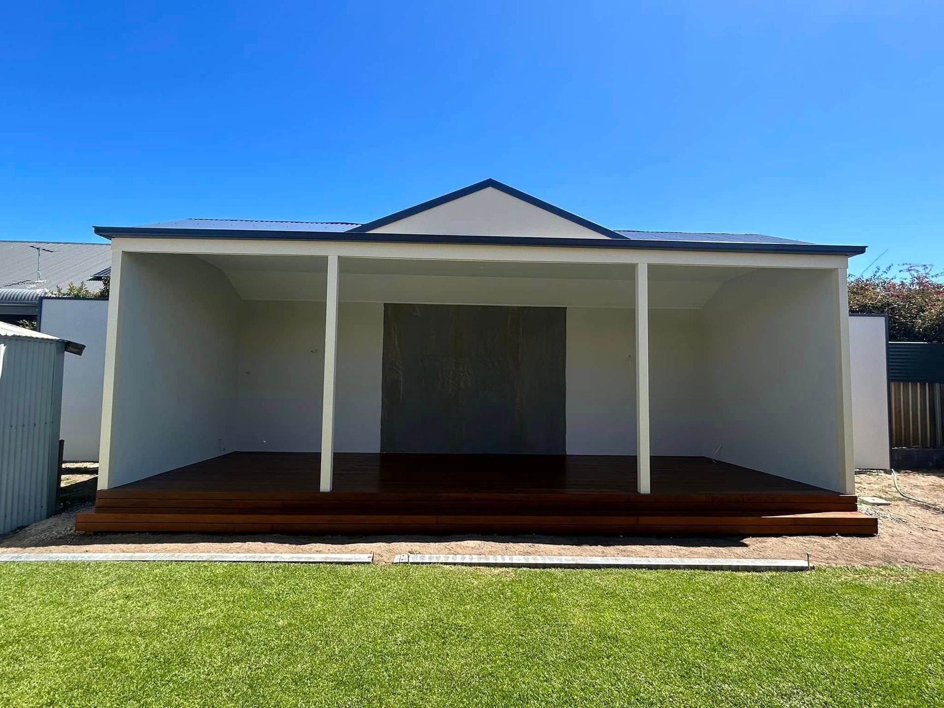 A paved walkway beside a brick wall, leading to a garden area covered by a corrugated metal patio roof.