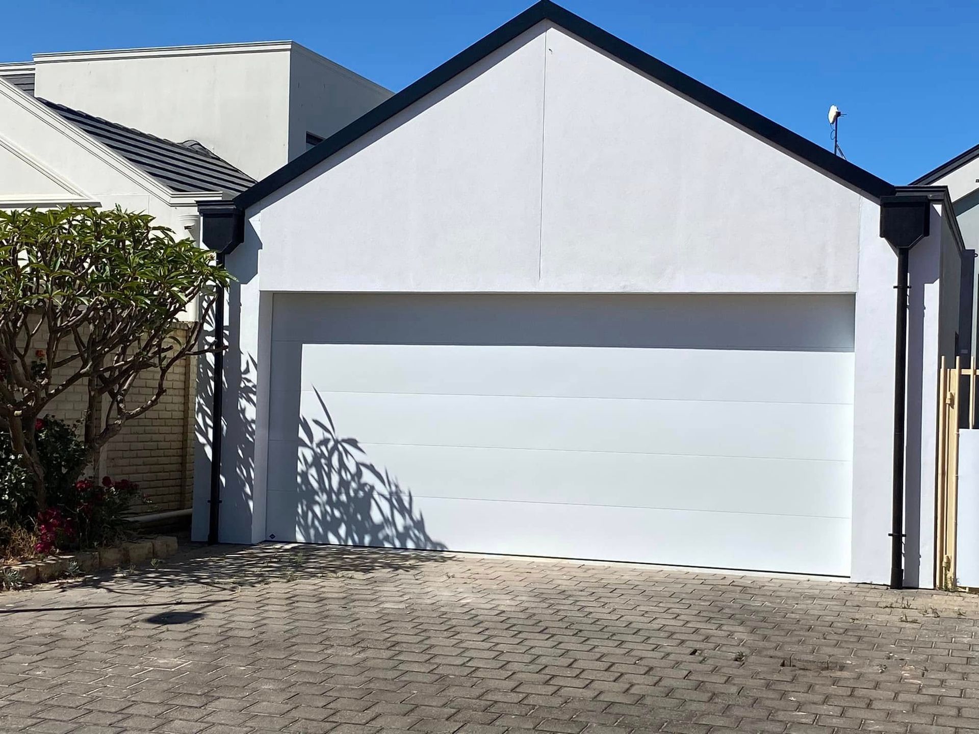 A gray sedan parked under a covered carport next to a suburban house with a brick wall and green landscaping.